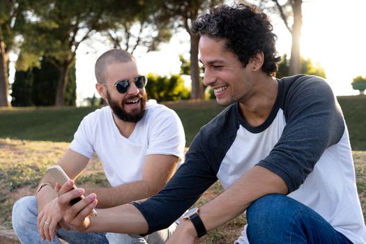 Two friends having fun with mobile in the park at sunset