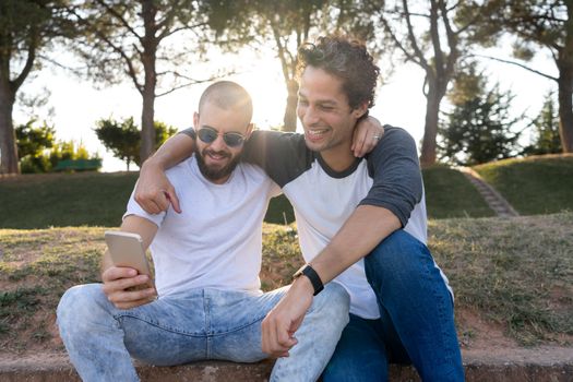 Two friends having fun with mobile in the park at sunset