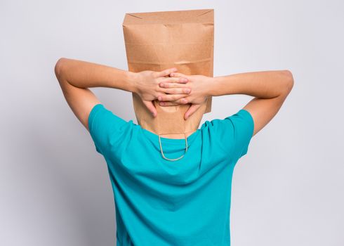 Portrait of teen boy - back view, with paper bag over head taking rest, on gray background. Time to relax. Child holding hands behind his head having time-out - rear view.