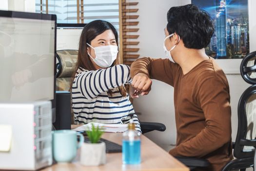 Couple of Asian colleagues wearing the surgical mask and elbows bump with partnership together before working in Home office when Covid-19 pandemic,Coronavirus outbreak,new normal concept