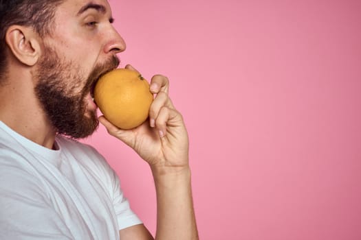 Young man with orange on a pink background in a white t-shirt emotions fun gesticulating with model hands. High quality photo