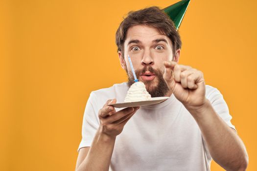 Handsome man with a beard and in a cap celebrating a birthday party yellow background. High quality photo