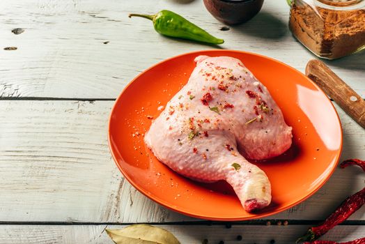 Chicken leg quarter on orange plate over wooden surface with different spices