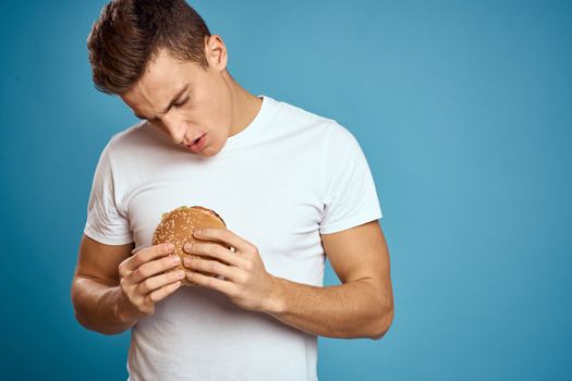 man with hamburger and white t-shirt blue background emotions gesturing with hands Copy Space. High quality photo