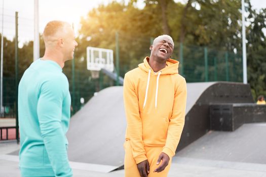 Multi-ethnic friendship Black african-american and caucasian guy friends spending time together on skate park Two multi ethnic student Dressed colorful sportswear.