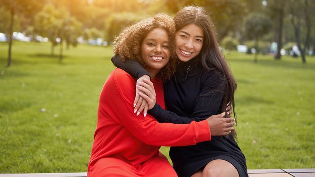 Diversity and feminity concept. Happy smiling Confident young mixed race women sitting bench park outdoor Asian and african american female resting on nature summer day