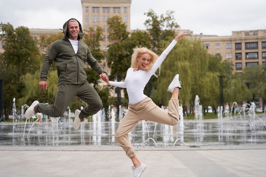 Couple in love walking outdoors park fountain Caucasian man woman walk outside after jogging dressed sport clothes Healthy livestyle Positive emotions happy jumping