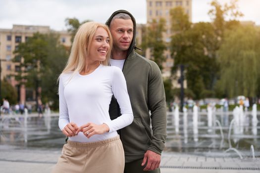 Couple in love walking outdoors park fountain Caucasian man woman walk outside after jogging dressed sport clothes Healthy livestyle dress up the hood