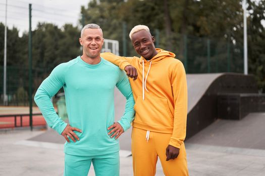 Multi-ethnic friendship Black african-american and caucasian guy friends spending time together on skate park Two multi ethnic student Dressed colorful sportswear.