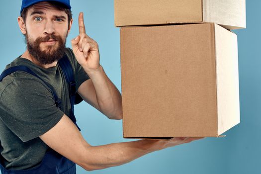 Man in working uniform with boxes in hands delivery service blue background. High quality photo