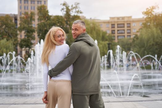 Couple in love walking outdoors park fountain Caucasian man woman walk outside after jogging dressed sport clothes Healthy livestyle Rear view