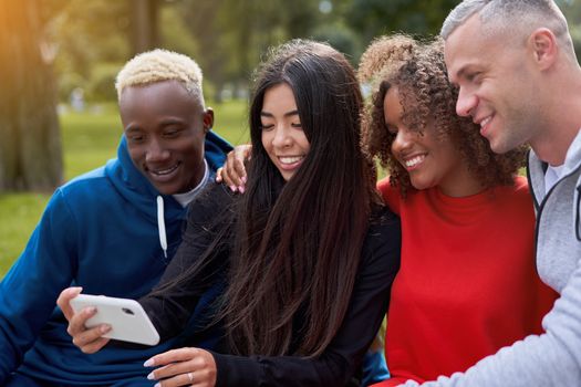 Multi ethnic friends outdoor taking a selfie on smartphone. Diverse group people Afro american asian spending time together Multiracial male female student sitting bench park outdoors