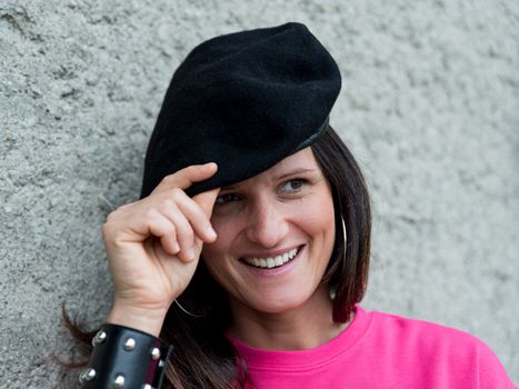 Close up portrait of smiling girl wearing a black beret and a fuchsia dress and a studded bracelet, narrow image of woman on light background