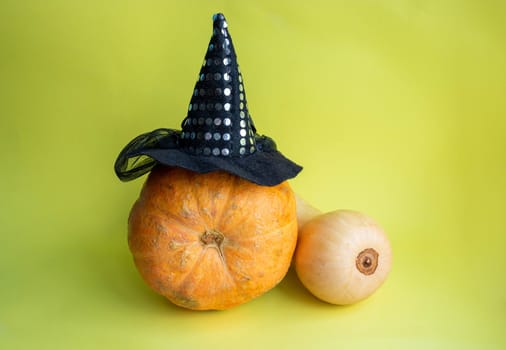 The Concept Of Halloween. An orange pumpkin in a witch's hat and a long yellow pumpkin on a yellow background.