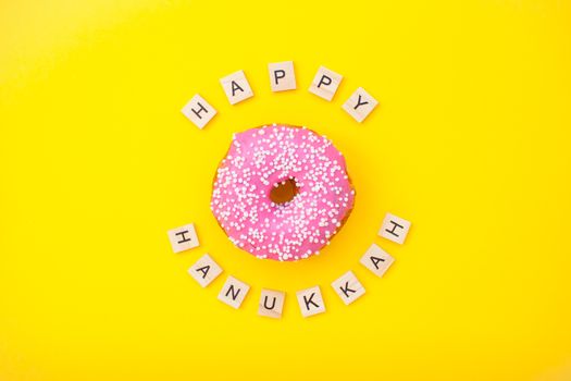 Bright pink delicious donuts on yellow background and inscription from wooden blocks happy hanukkah