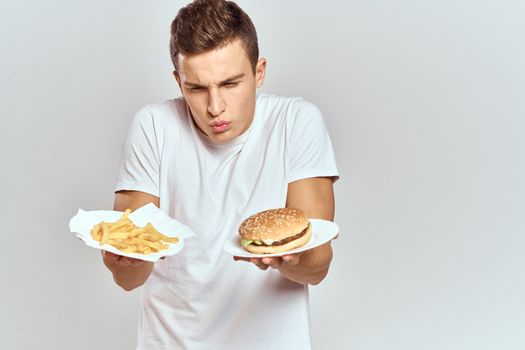 a man with fries and a hamburger on a light background in white t-shirt close-up cropped view Copy Space Model. High quality photo