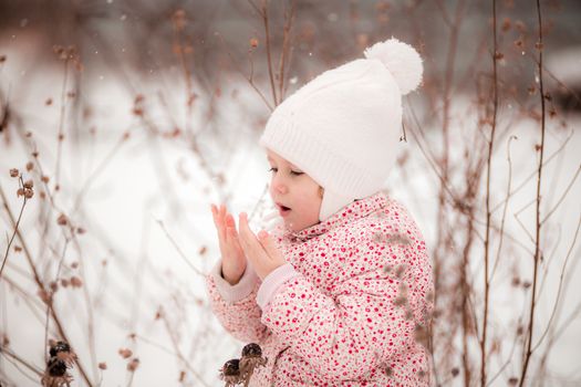 .A little girl sits in the snow and warms her frozen hands with her breath