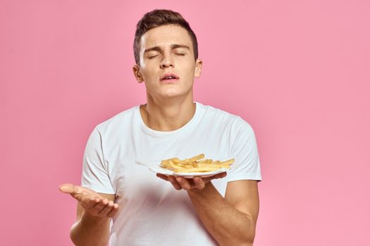 Man with French fries in a paper box on a pink background calories fast food portrait pink background. High quality photo