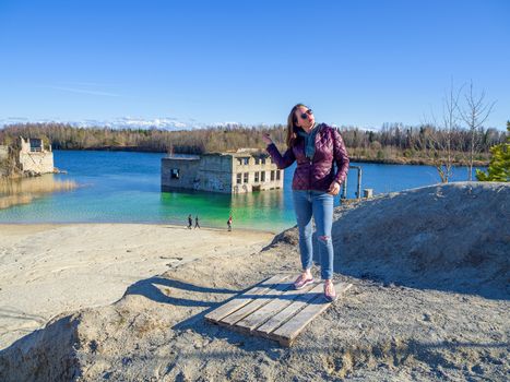 Hiker on mountain top. Woman is standing with an Abandoned Quarry and water on the background. Scenic View Of Land Against Clear Blue Sky. Panoramic View.