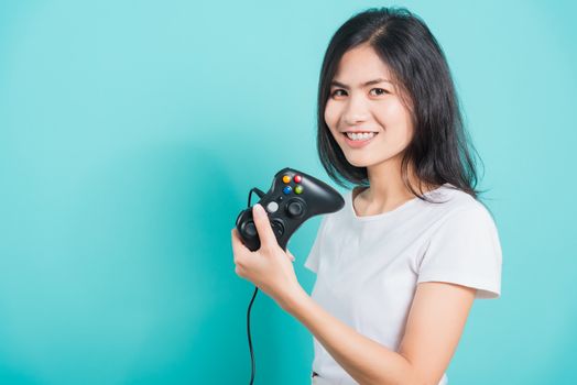 Portrait Asian beautiful happy young woman wear t-shirt gamer with a joystick or gamepad in hands, on blue background, with copy space