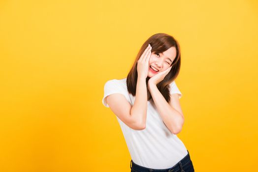 Asian happy portrait beautiful cute young woman teen stand surprised excited celebrating open mouth gesturing palms on face looking to camera isolated, studio shot yellow background with copy space