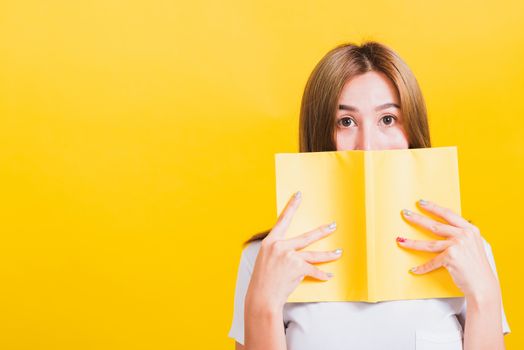 Portrait Asian Thai beautiful happy young lifestyle woman stands holding yellow book or diary her looking to camera, studio shot isolated on yellow background, with copy space