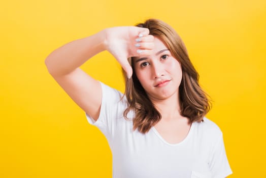 Portrait Asian Thai beautiful young woman unhappy, a negative gesture showing finger thumbs down or dislike sign, studio shot isolated on yellow background, There was copy space, rejection concept