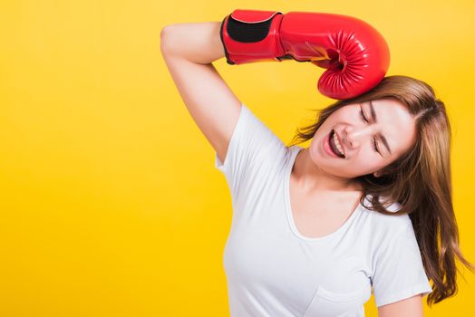 Portrait Asian Thai beautiful young woman standing smile in red boxing gloves punch head and close eyes, shoot the photo in studio shot isolated on yellow background, There was copy space for text