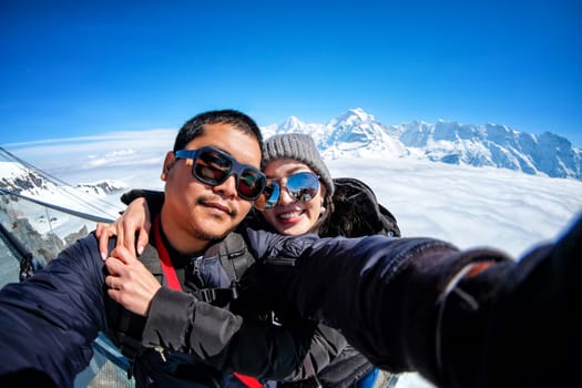 Young Couple Tourists selfie with mobile phone near view of the Swiss Skyline from Schilthorn, Switzerland