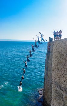 Acre, Israel - September 14, 2020: Young Arab man jumps from the old city wall to the sea, with others watching, in Acre (Akko), Israel. Multiple stages of the same jump