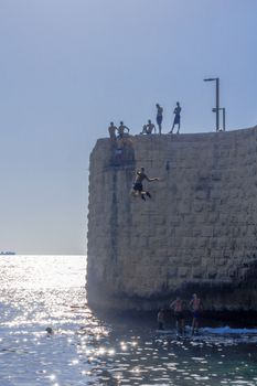 Acre, Israel - September 14, 2020: Young Arab man jumps from the old city wall to the sea, with others watching, in Acre (Akko), Israel