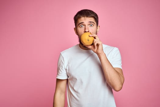 Young man with orange on a pink background in a white t-shirt emotions fun gesticulating with model hands. High quality photo