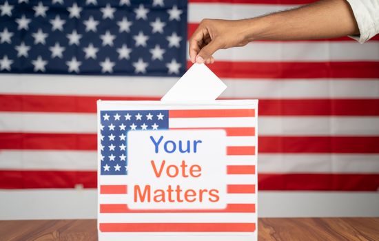 Close up of Hands placing vote inside the Ballot box with your vote matters printed with US flag as background - Concept of voter rights and US election