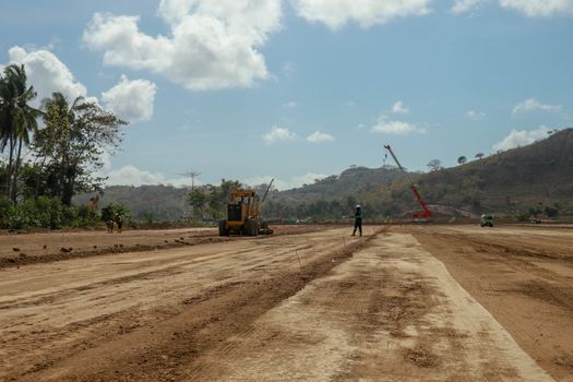 Working machines and heavy equipment adjust the terrain of the race track. Construction of the area and the Moto GP Mandalika racing circuit, West Nusa Tenggara, Lombok, Indonesia. Building a racetrack for motorcycles.