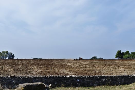 Ploughing the fields with old tractor against bright sky ,in the foreground a wall