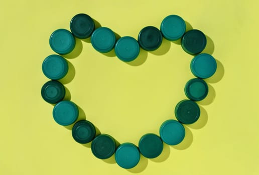 Green plastic bottle caps forming heart shape on yellow background