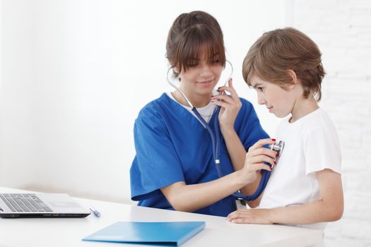 healthcare and medical concept - young female cardiologist doctor with stethoscope listening to child chest heartbeat in hospital