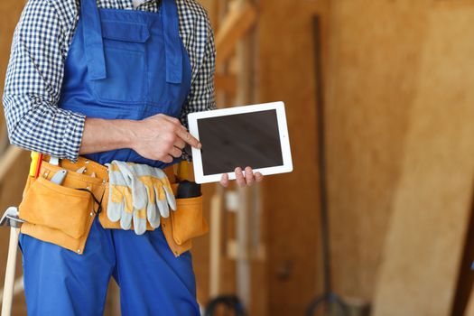 Construction worker at site pointing at blank digital tablet pc with copy space for text