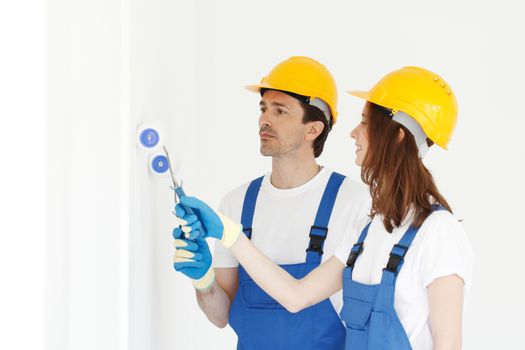 Two young workers in uniform of coverall and hardhat painting white wall