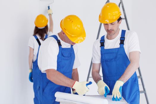 Building, renovation, repair, teamwork and people concept - close up of builders discussing blueprint indoors woman painting wall on backround