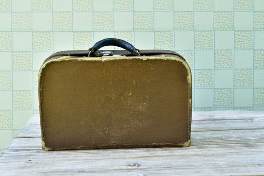 old suitcase stands on a shabby wooden table against the background of retro wallpaper