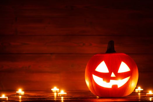 Halloween Jack o Lantern pumpkin head and burning candles on wooden background