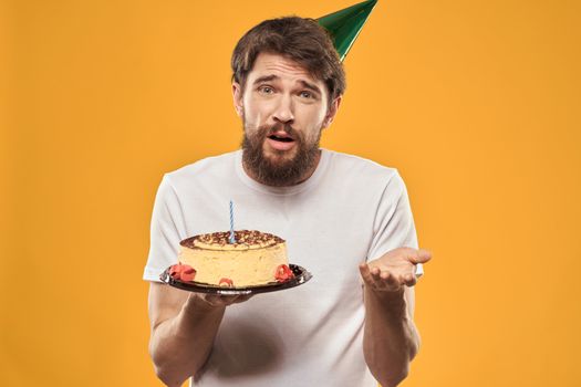 Handsome man with a beard and in a cap celebrating a birthday party yellow background. High quality photo