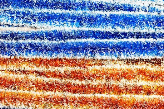 The texture and background of fluffy New Year's Christmas tinsel in blue and orange in horizontal stripes divides the picture in half.