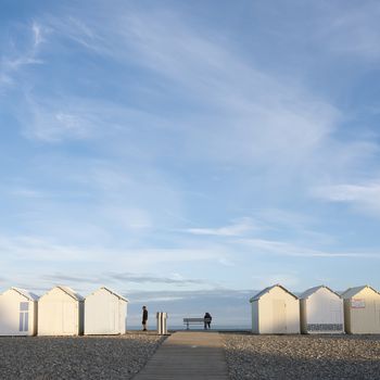 cayeux, france, 6 august 2020: people near beach huts in cayeux s mer in french normandy under blue sky in early morning sunlight