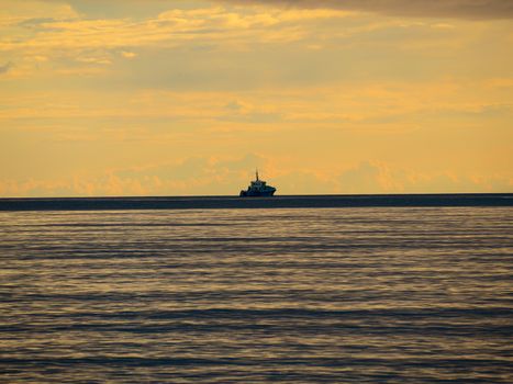 One small fishing boat heading out on the foggy ocean at dawn. Boat on the background of sunset. The Baltic Sea close up, stormy dramatic dark clouds. The Vacation, summer concept