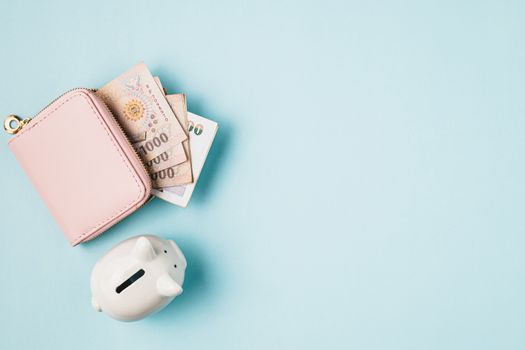 Saving piggy bank with wallet of Thai currency, 1000 Baht, money banknote of Thailand on blue background for business and finance concept