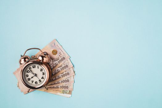 Bell alarm clock  with Thai currency, 1000 Baht, money banknote of Thailand on blue background for business, finance and time management concept