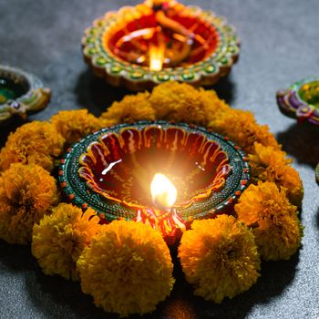 Close up clay lit light a fire already on Diya or oil lamp with flowers, studio shot on concrete background, Decoration of Hinduism rangoli, Happy celebration Deepavali or Diwali Indian festival concept