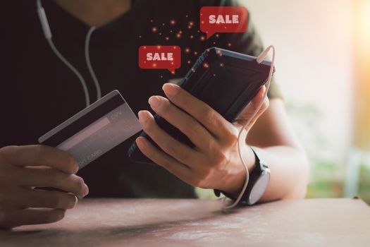 Shopping online concept. Hand holding black smartphone with red popup sale icon and credit card. Black Friday and shop at home.